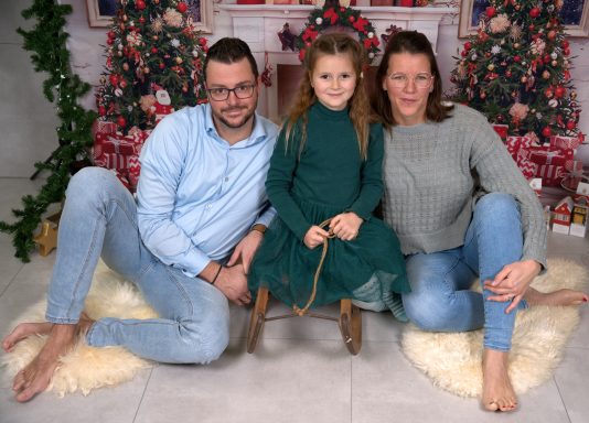 Familie sitzt zusammen auf einem Teppich vor weihnachtlicher Dekoration.