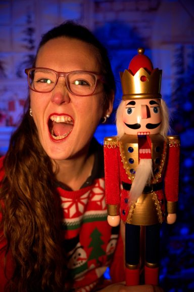 Junge Frau mit Brille hält einen Nussknacker und lächelt begeistert.