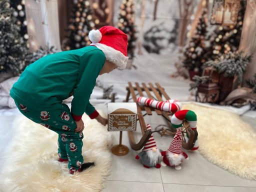 Ein Kind in grüner Weihnachtskleidung spielt mit Dekorationen und Wichteln in einem festlichen Raum.