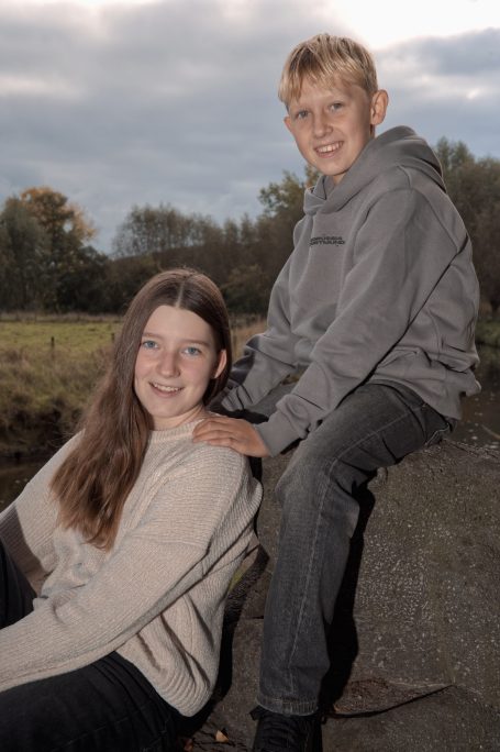 Ein Mädchen sitzt auf dem Boden, während ein Junge hinter ihr steht, beide lächeln.