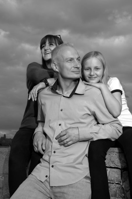 Familie posiert lächelnd vor einem bewölkten Himmel.