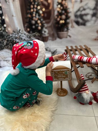 Ein Kind in Weihnachtskleidung spielt mit einem Schlitten und Dekoration im Winterambiente.