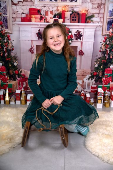 Ein lächelndes Mädchen in einem grünen Kleid sitzt vor einer festlichen Kulisse.