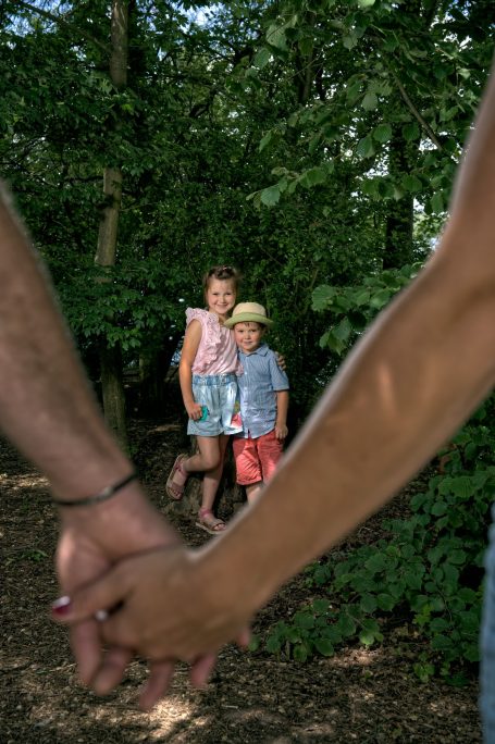 Zwei Erwachsene halten Händchen im Vordergrund, während Kinder im Hintergrund stehen.