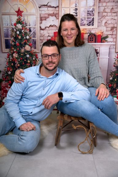 Ein Paar posiert in winterlicher Dekoration, lächelnd und entspannt in bequemer Kleidung.