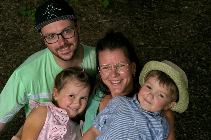 Familie mit zwei Kindern lächelt gemeinsam in der Natur.