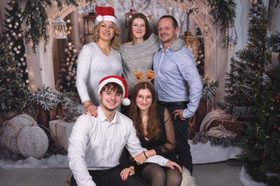 Fünf Personen in festlicher Kleidung, umgeben von Weihnachtsdekoration.